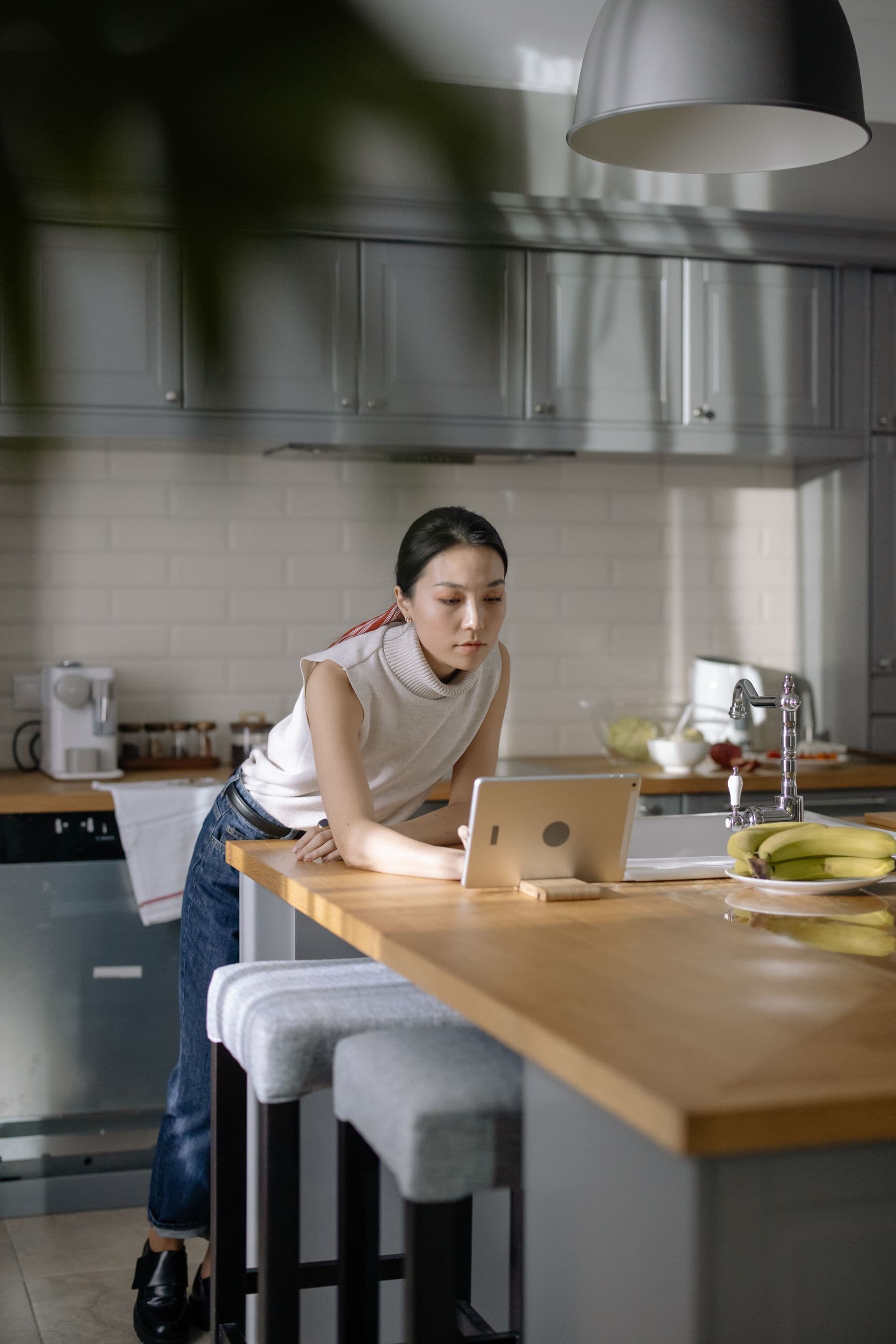 A woman leaning on her kitchen counter, reading something on a tablet