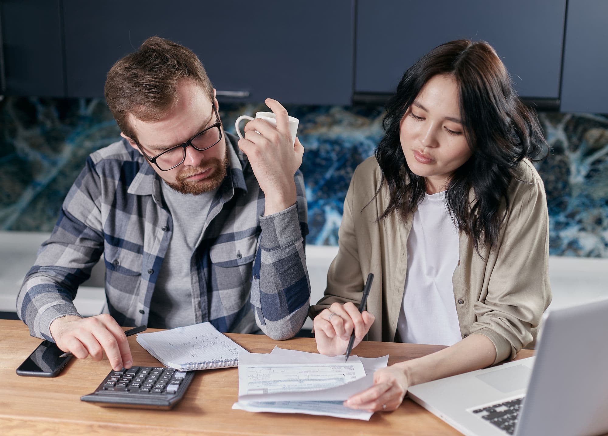 Two people at a kitchen table going through household bills with a calculator